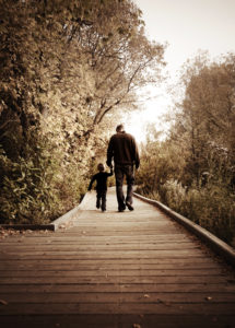 A father and child walk in the distance down a nature path.