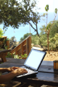 A person sits on a porch outside and works on a laptop.