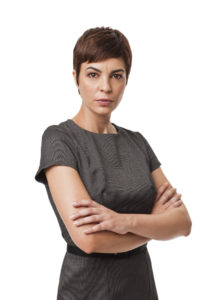 A business woman in a dress crosses her arms sternly and confidently.