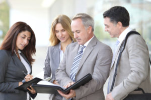 Four business people stand around looking at a document being held by an older business man.