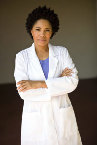 A woman wearing a lab coat crosses her arms and looks into the camera.