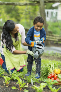 A mother and her child water plants in their garden together.