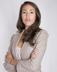 A young woman in a business suit crosses her arms and looks confidently at the camera.