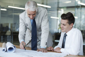 Two male architects are leaning over a drawing in a professional setting.