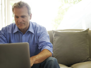 A mature man works on a laptop while sitting on a couch