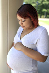A pregnant woman is holding her stomach and smiling at it.