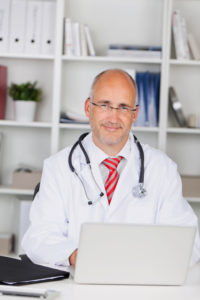 A male doctor looks at the camera, in his white coat and stethoscope.
