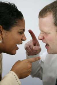 A man and a woman are in a heated argument. Their faces are close and they are pointing at each other fiercely.