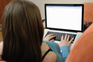 A woman is typing on her laptop. The screen is blank.