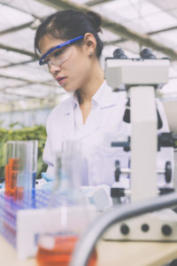 A female scientist looks at test tubes next to a microscope.