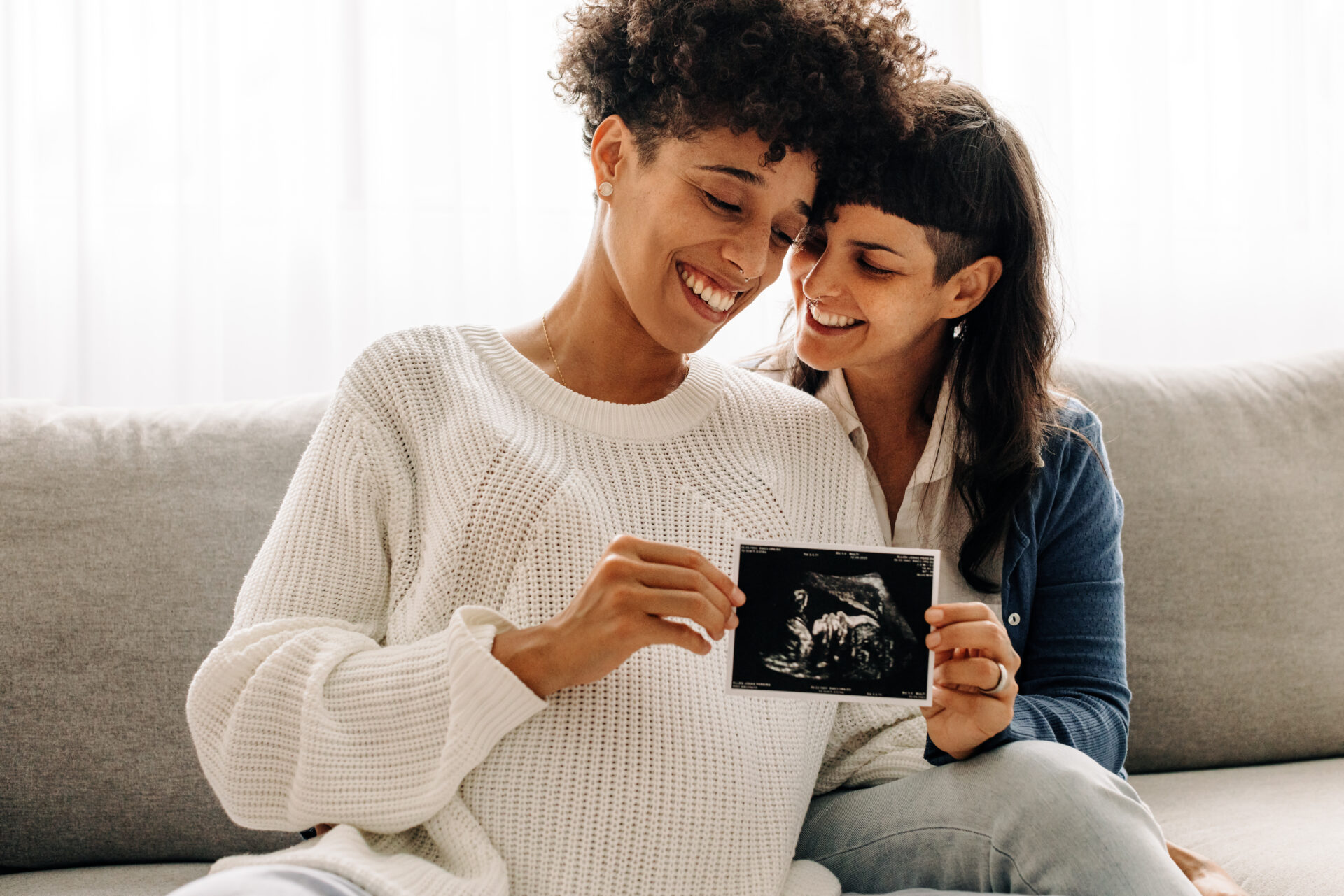 Same-sex pregnant couple holding up their ultrasound scan